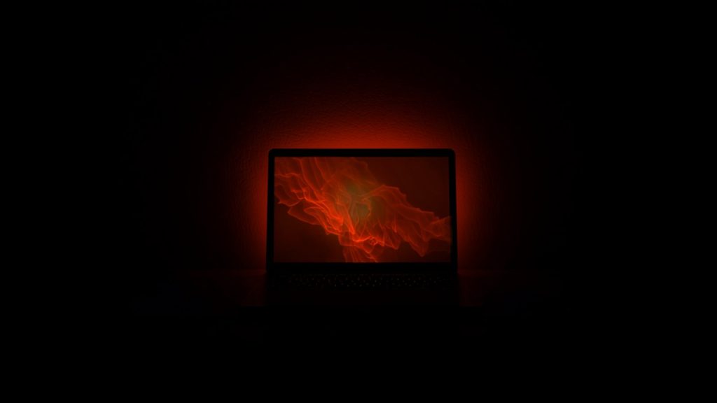 A laptop alone in a dark room throwing red light on the wall, a compromised website nobody is watching.